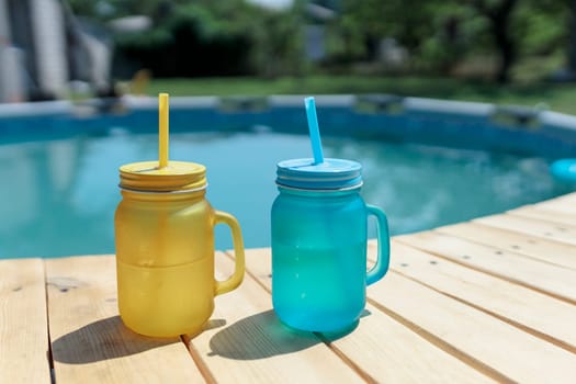 two cocktails of yellow and blue standing by the pool. Pool party outdoors.