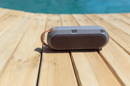 Modern portable music speaker with voice assistant near the swimming pool.