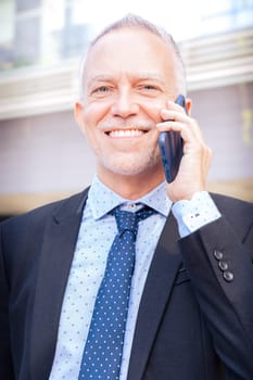 Satisfied with the results, the businessman walks down the street in front of the office building, a mature boss is talking on the telephone.Vertical