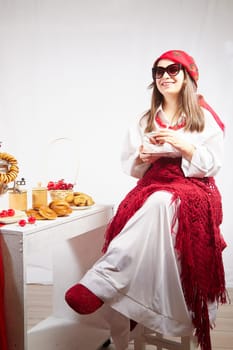 A fashionable modern girl in stylized folk clothes at table with a samovar, bagels and tea for the Orthodox holiday of Maslenitsa and Easter. Funny photo shoot for a young woman