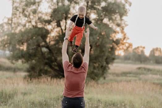 dad tosses up a happy son in a field in the summer. Added grain simulates film photo
