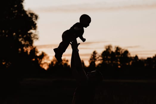 silhouette dad plays and throws his little son in the field in the summer at sunset. Added grain simulates film photo