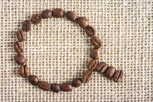 Coffee beans in the shape of a cup, on a burlap fabric. Background voor coffee related products.
