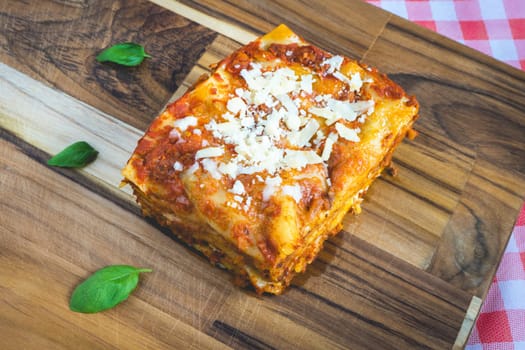 Top view from a homemade Lasagna, on a wooden cutboard, decorated with basil.