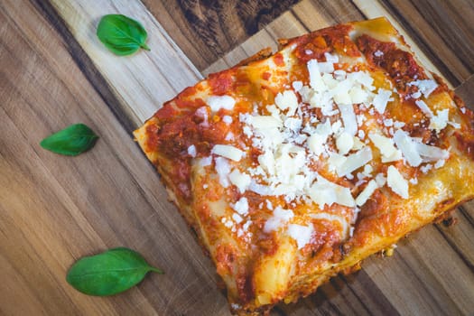 Top view from a homemade Lasagna, on a wooden cutboard, decorated with basil.
