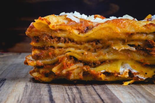 Close up view from a home made Lasagna, on a wooden table, and a dark background.