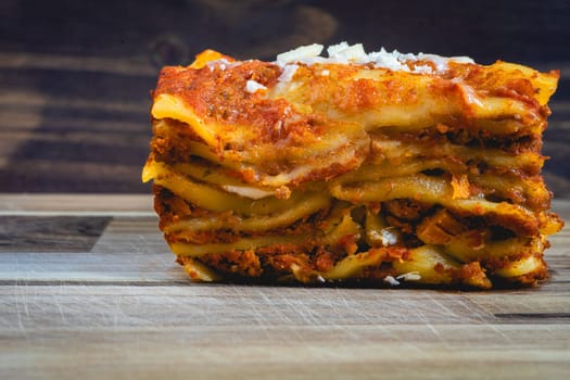 Close up view from a home made Lasagna, on a wooden table, and a dark background.