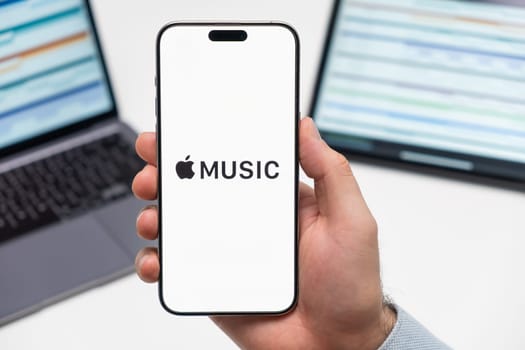 PRAGUE, CZECH REPUBLIC - JANUARY 21 2024: Apple Music logo on the screen of smartphone in mans hand on the workplace background.