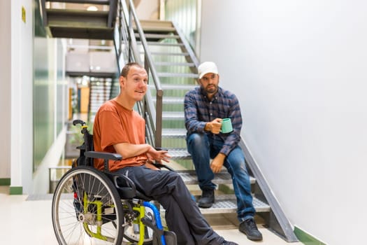 Man with cerebral palsy talking with a work colleague indoors in a modern coworking with staircase