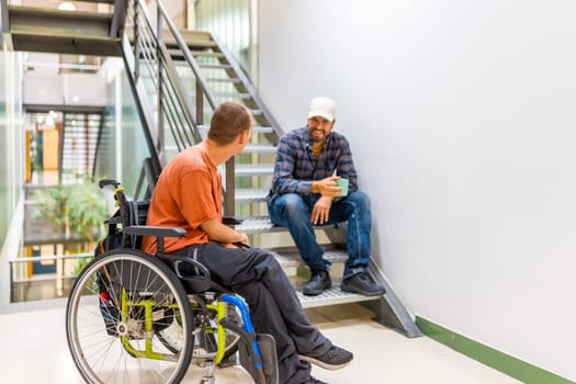 Man in wheelchair with a coworker during work break drinking coffee and chatting