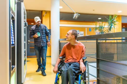 Coworkers walking into vending machines in a work break. One of them are a man with disability sitting on wheelchair