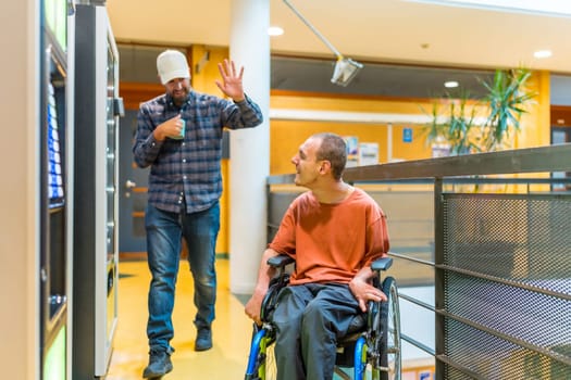 Man with disability and colleague chatting next to vending machine in a modern coworking