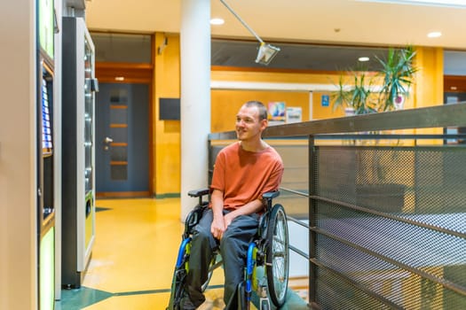 Disabled man sitting on a wheelchair looking into vending machine in a coworking