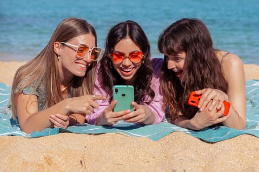 Group of smiling multiethnic women enjoying vacation. Beautiful and cheerful Gen Z girls with their mobile phones pose looking at the camera with a mobile phone.
