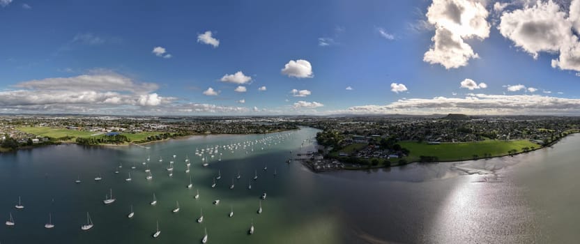 Drone shot of the Tamaki river with cloud reflections at sunset. Sailboats on moorings line up the river and marina in New Zealand