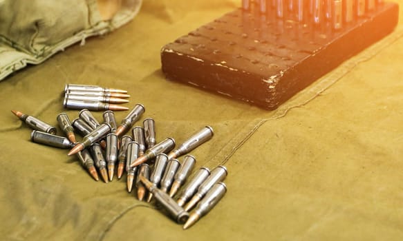 A soldiers hand is carefully reaching into a wooden box to hold a single bullet, while scattered bullets are arranged on an olive drab cloth surface, creating a compelling sense of depth and focus.