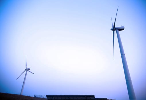 A cluster of wind turbines stand tall against a clear blue sky, their blades spinning energetically to harness wind power for energy generation.