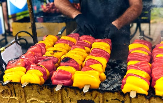 Colorful bell peppers on skewers grilling outdoors, sizzling and charred. A delicious smoky aroma fills the air, creating a vibrant and appetizing scene for a summer barbecue gathering.