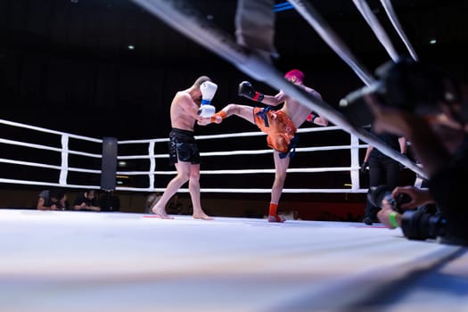 A man in a white glove is kicking another man in a boxing ring, fighting