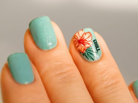Aesthetic visual of fingernail with short nail with blue green manicure with reverse stamping summer tropical flower. Nail closeup with stylish pink flower in reverse stamping nail art design manicure