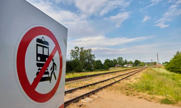 A concrete railway track under a sunny sky with a vivid prohibition sign displaying a train and a person, emphasizing no crossing. The scene captures rail safety on a lovely day.