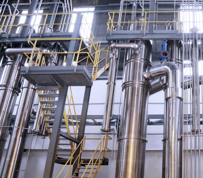A chemical plant features a complex network of stainless steel pipes and glass vessels, creating an intricate system of interconnected straight and curved components in various sizes and shapes.