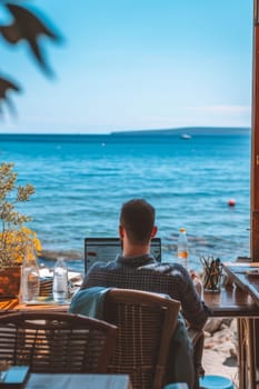 A person working on a laptop by the sea, surrounded by nature, under a clear sky