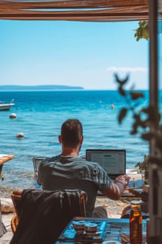 A person working on a laptop by the sea, surrounded by nature, under a clear sky
