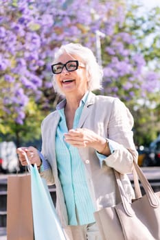 lively mature woman smiling happy walking through the city with shopping bags, concept of urban and active lifestyle in adulthood, copyspace for text