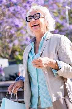 portrait of a lively mature woman smiling happy walking through the city with shopping bags, concept of urban and active lifestyle in adulthood