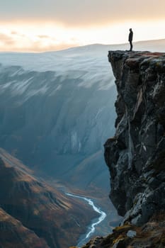 Person in red standing on a high cliff edge with a breathtaking view of a river and mountains during sunset