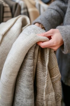Hand gently selecting a woolen knit from a pile of cozy, handcrafted sweaters
