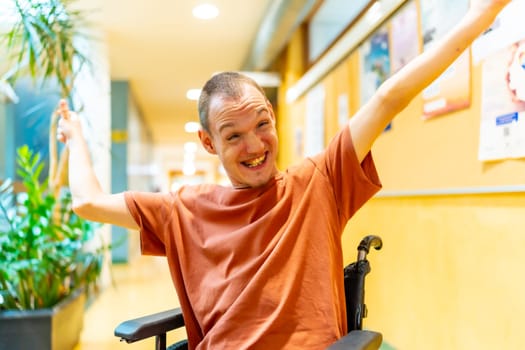 Proud man with disability celebrating in the university sitting on wheelchair and raising arms smiling at camera