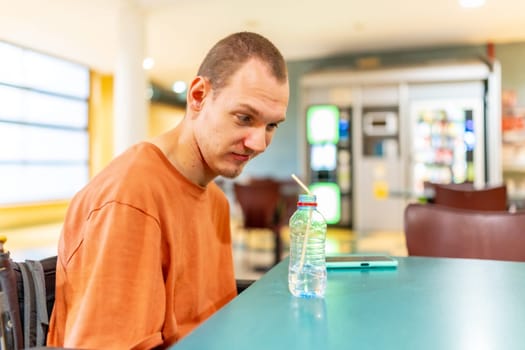 Man with cerebral palsy drinking water with straw sitting alone in a coworking cafeteria