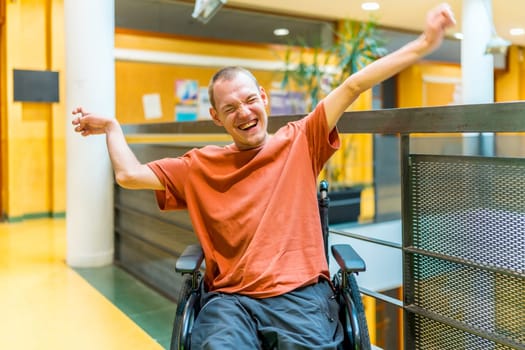 Successful man with disability celebrating in a modern coworking sitting on wheelchair and raising arms while smiling alone