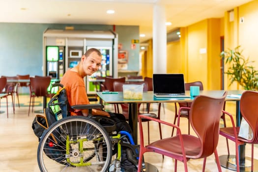 Horizontal full lenght photo of a caucasian adult man with disability in wheelchair in a dinning room in coworking