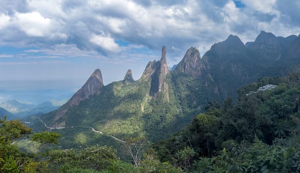 Panoramic landscape with towering mountains, lush greenery, and a dramatic sky.