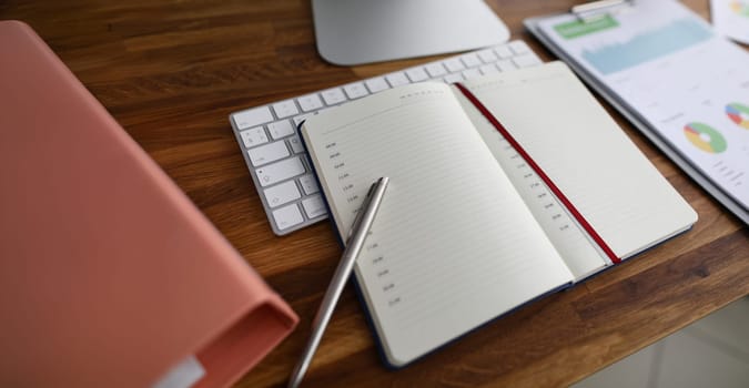 Business worker workplace in bureau. Keyboard, paper folder with important statistics documents, notepad and pen lying on wooden table. Empty copy space in daily planner
