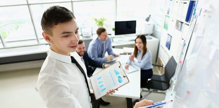 Young handsome teacher man in suit with workgroup seminar board with chart coaching background. Lecturer for applicants retraining financial statistics management enterprise etiquette corporate spirit