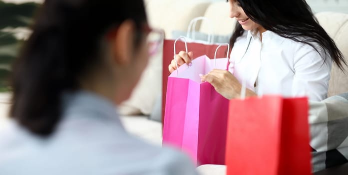 Focus on colorful packets of smart businesswoman sitting indoors. Wopk assistant discussing with colleague fashion shopping sale. Shopping concept. Blurred background