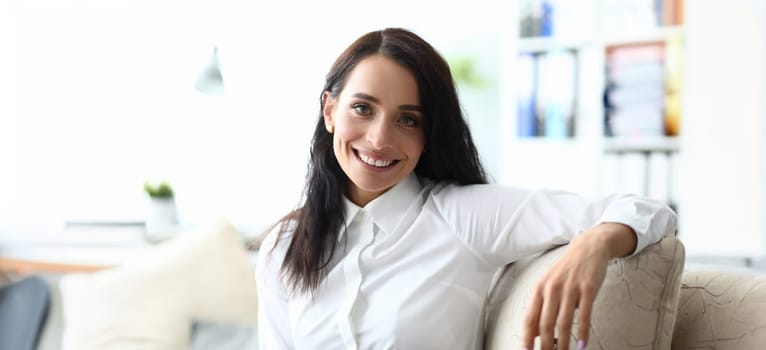 Portrait of beautiful businesswoman sitting on comfortable sofa and posing at camera with happiness. Smiling woman relaxing on comfy office furniture. Hardworking lady worker concept