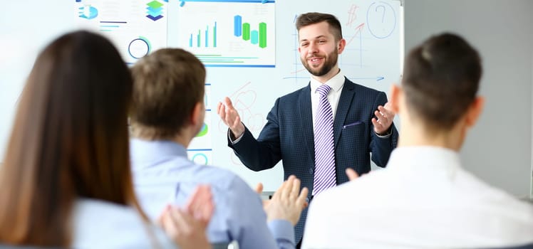 Young handsome teacher man in suit with workgroup seminar board with chart coaching background. Lecturer for applicants retraining financial statistics management enterprise etiquette corporate spirit