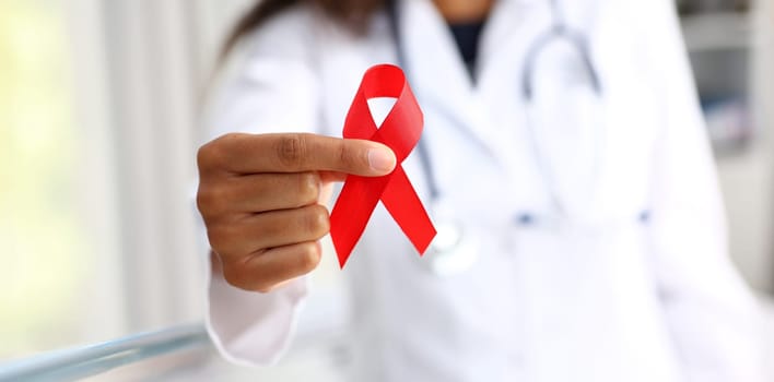 Black woman doctor holding a red ribbon in his hand an international day of protecting people from cancer by symbol of struggle and survival mankind