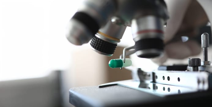 Focus on metallic tweezers holding drugs. Laboratory research of marijuana medicines under microscope. Medicine and healthcare concept. Blurred background