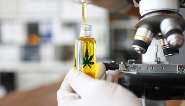 Focus on male hand holding glass bottle with cannabinoid oil. Pharmacist dripping medicine drops in flask. Healthcare and marijuana concept. Blurred background