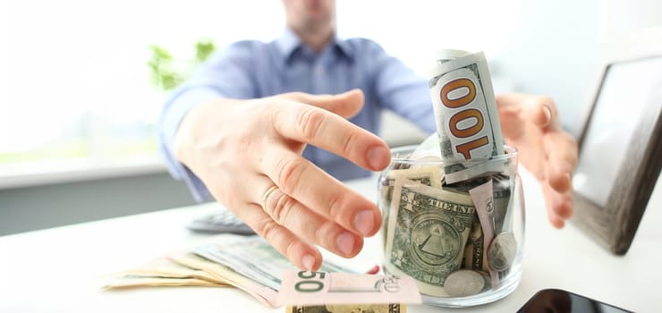 Male hands grabbing big fat jar full of US currency as greed gesture closeup