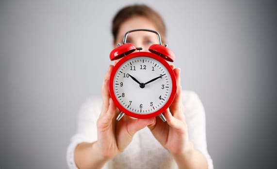 Adult smiling caucasian woman hold red alarm clock on gray background.