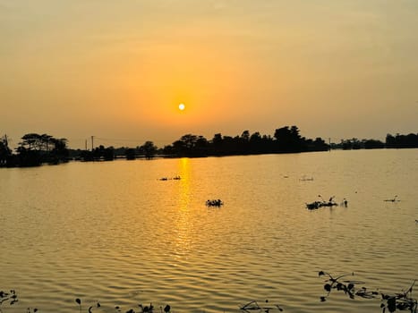 A breathtaking view of the sun setting over a tranquil lake, casting warm hues across the water and sky. This stunning scene is perfect for use in romantic, nature, and landscape projects.