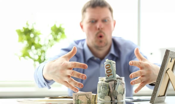 Male hands grabbing big fat jar full of US currency as greed gesture closeup
