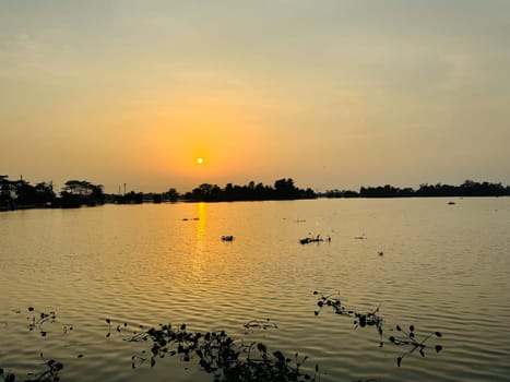A breathtaking view of the sun setting over a tranquil lake, casting warm hues across the water and sky. This stunning scene is perfect for use in romantic, nature, and landscape projects.